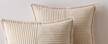 Two Act Design Shop crèmekleurige kussens met textuur en verticale en horizontale ribbelpatronen tegen een lichtgrijze muur.
