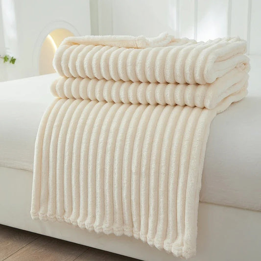 Een stapel netjes opgevouwen Deken Easing Soft Rib Beige handdoeken van Act Design Shop, geplaatst op een wit bed of bank, met de nadruk op een schone en serene sfeer.