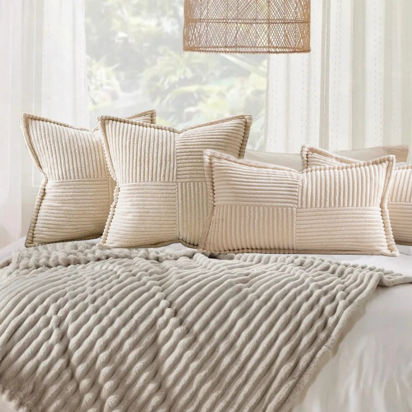 Een knus slaapkamertafereel met een reeks crèmekleurige getextureerde Act Design Shop neksteunkussens 30x50cm + vullingen op een gebreide sprei, tegen een achtergrond van heldere ramen met vitrages.
