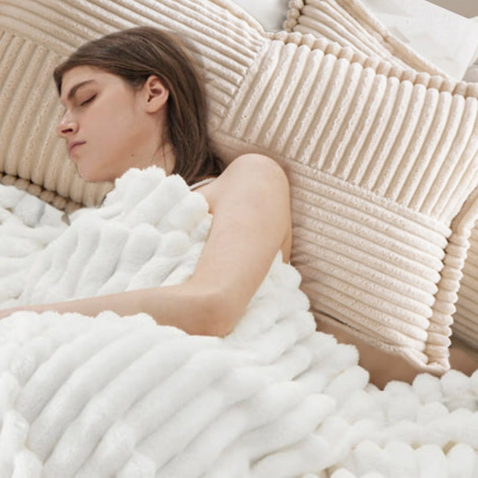 Een vrouw slaapt vredig, gedeeltelijk bedekt door een witte deken met textuur, terwijl haar hoofd rust op het neksteunkussen van Act Design Shop 30x50cm + vullingen in een zachte, lichte omgeving.